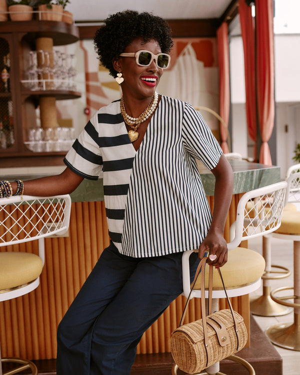 Woman in a black and white striped shirt and sunglasses standing in a retro-style room with orange curtains and vintage decor.
