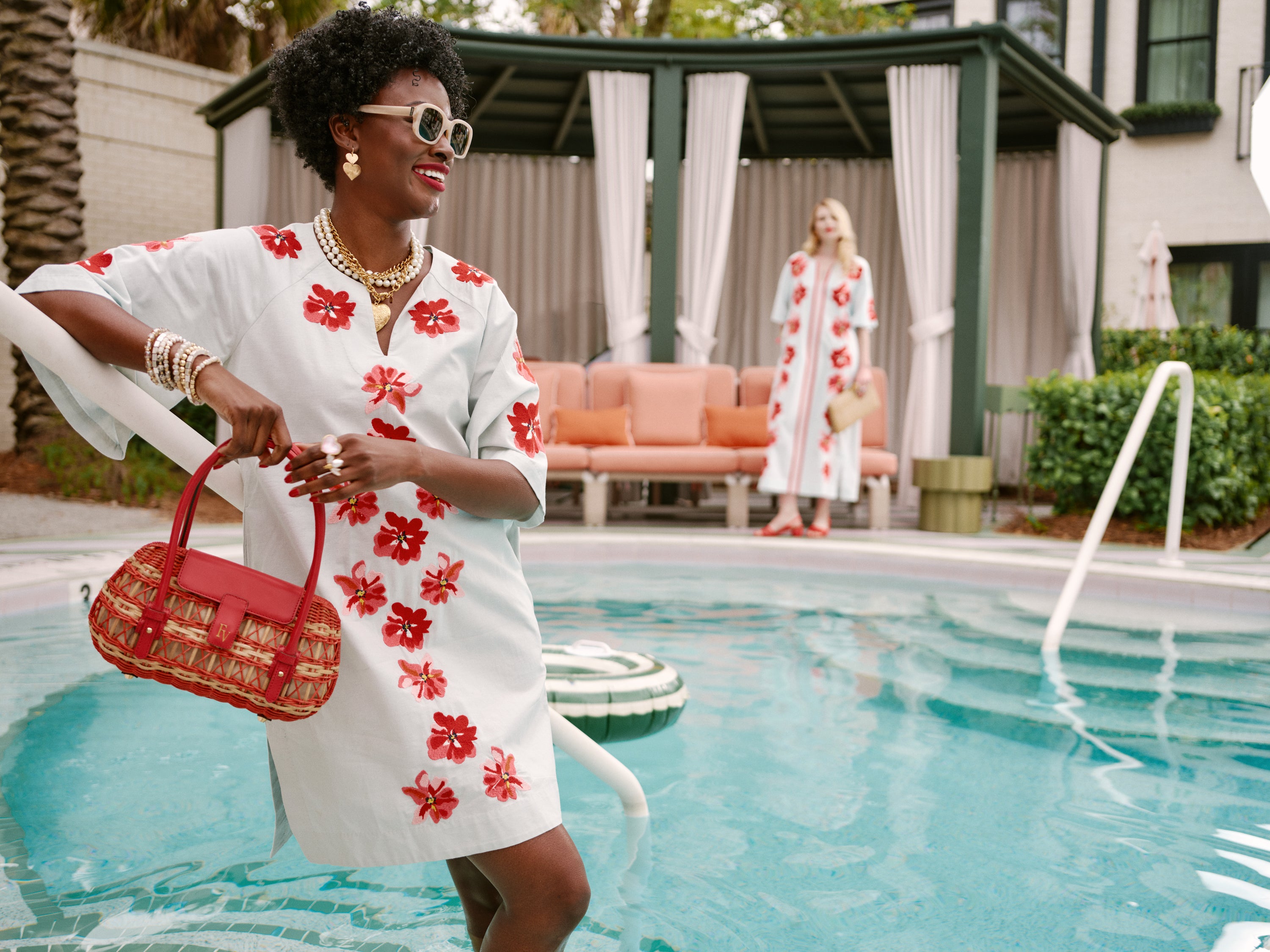 Woman in a white dress with red floral patterns by a poolside.