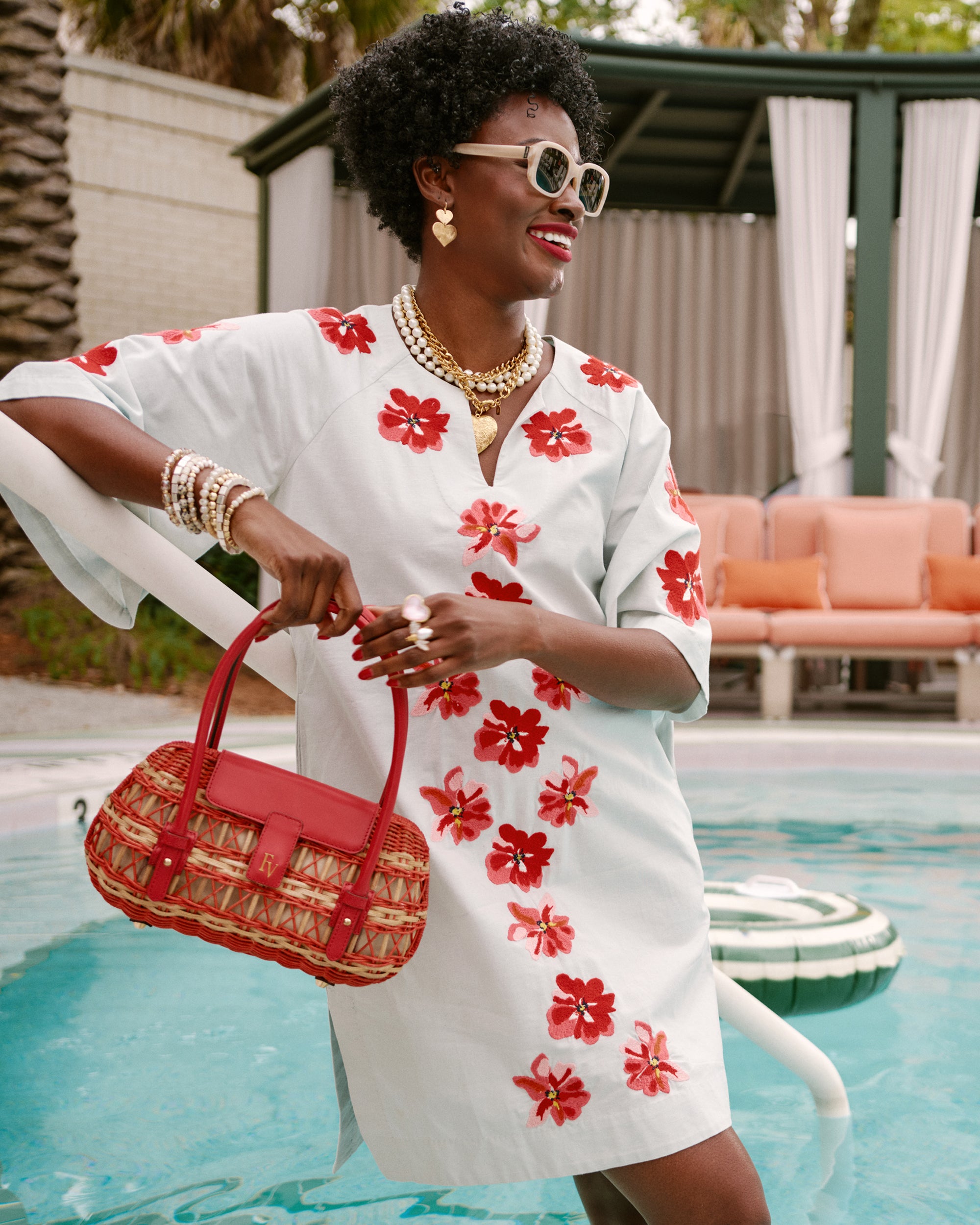 Woman in a white dress with red floral patterns by a poolside.