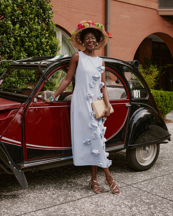 Woman in a light blue floral dress standing next to a vintage red car