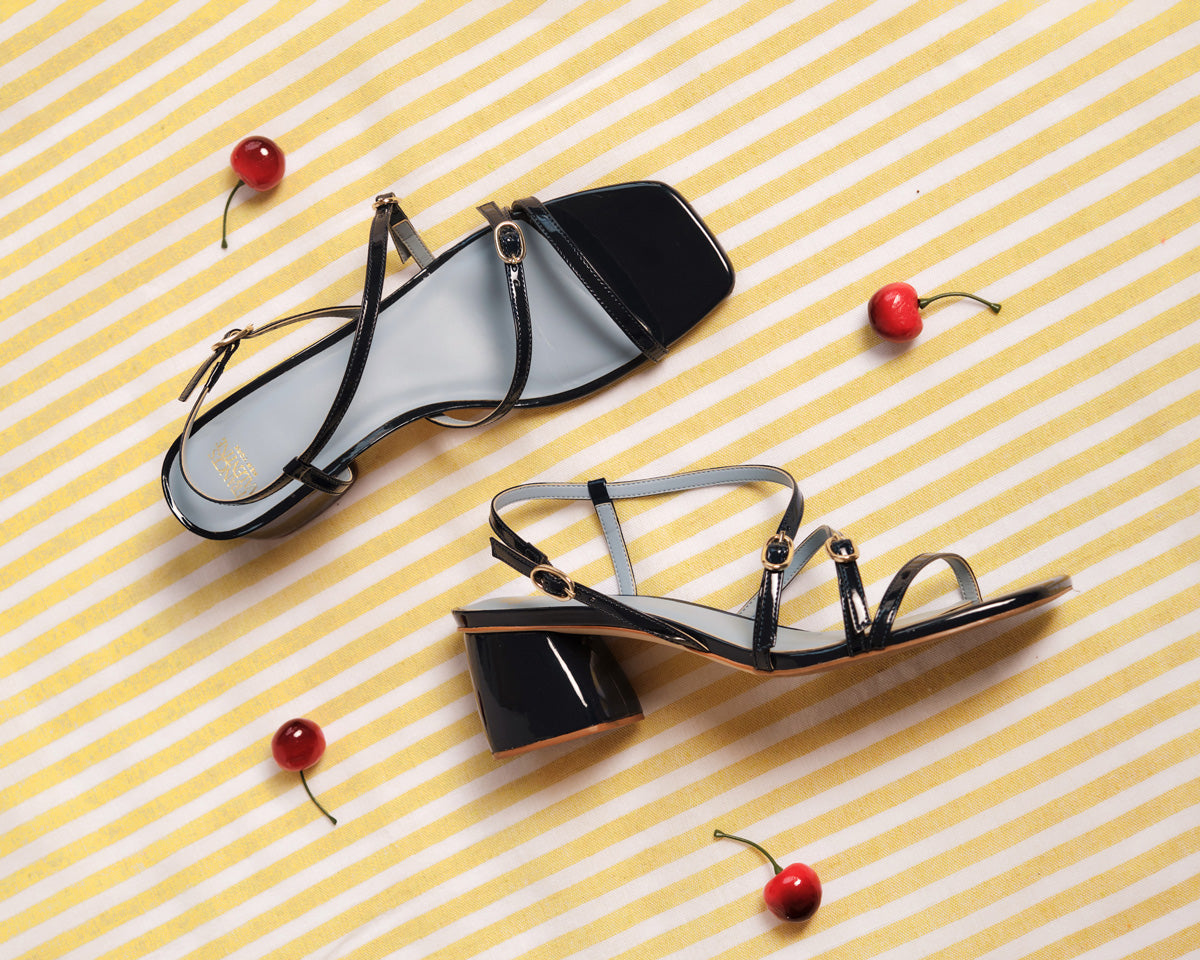 Black high-heeled sandals on a yellow and white striped background with cherries.
