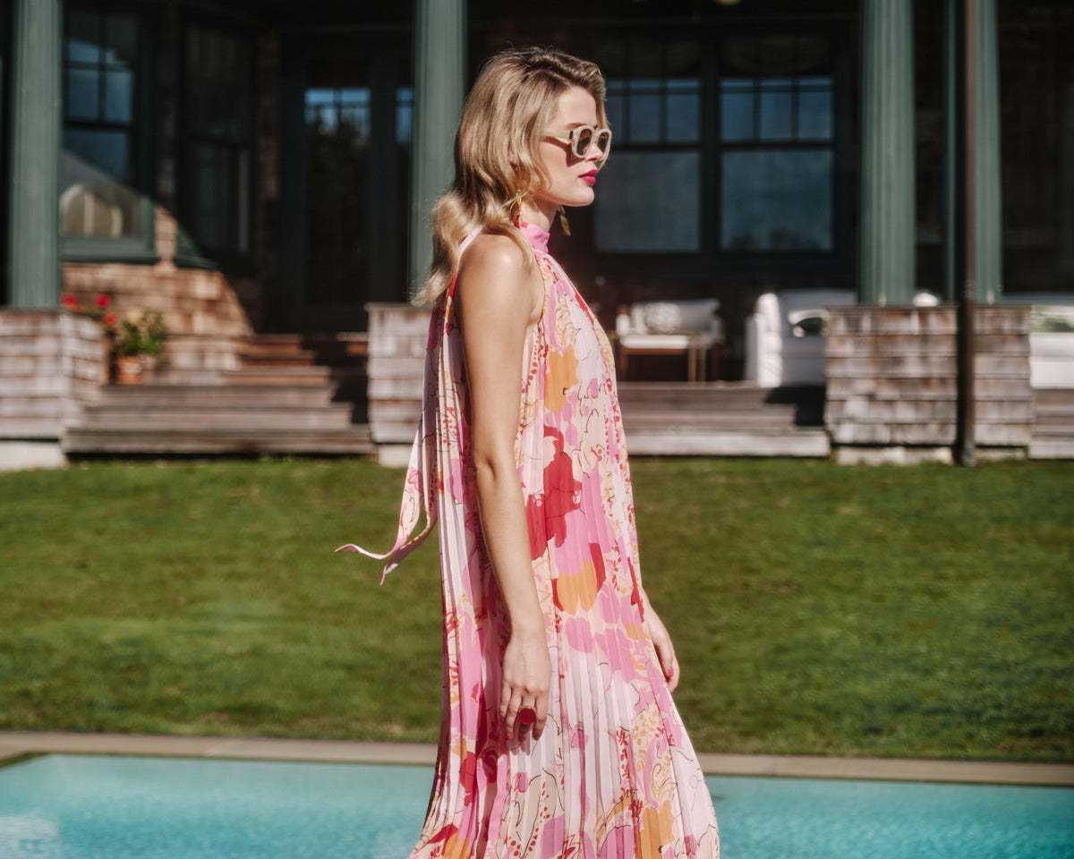 Woman in a floral dress standing by a pool with a house in the background